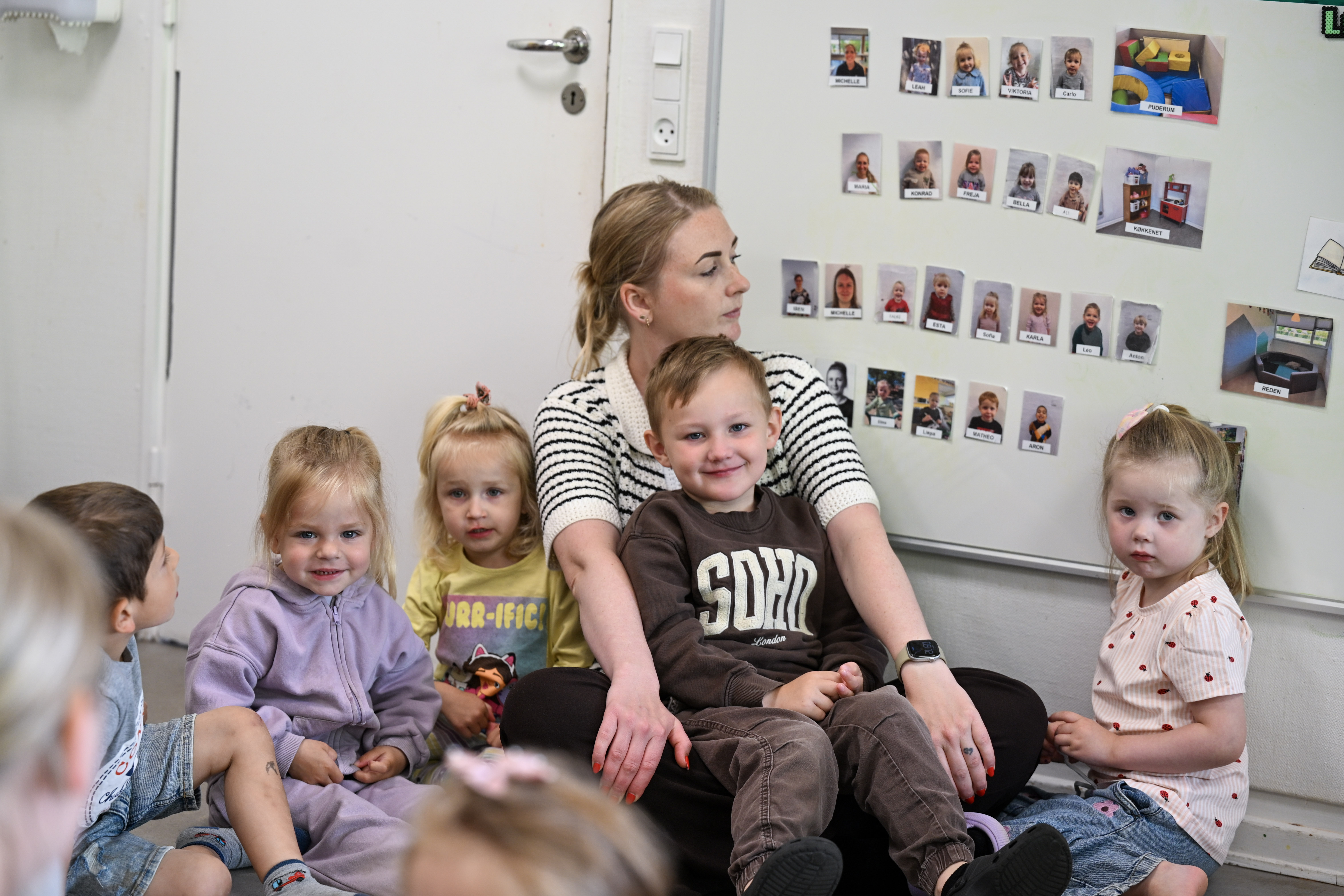 Voksen og børn ved tavle med billeder af alle voksne og børn